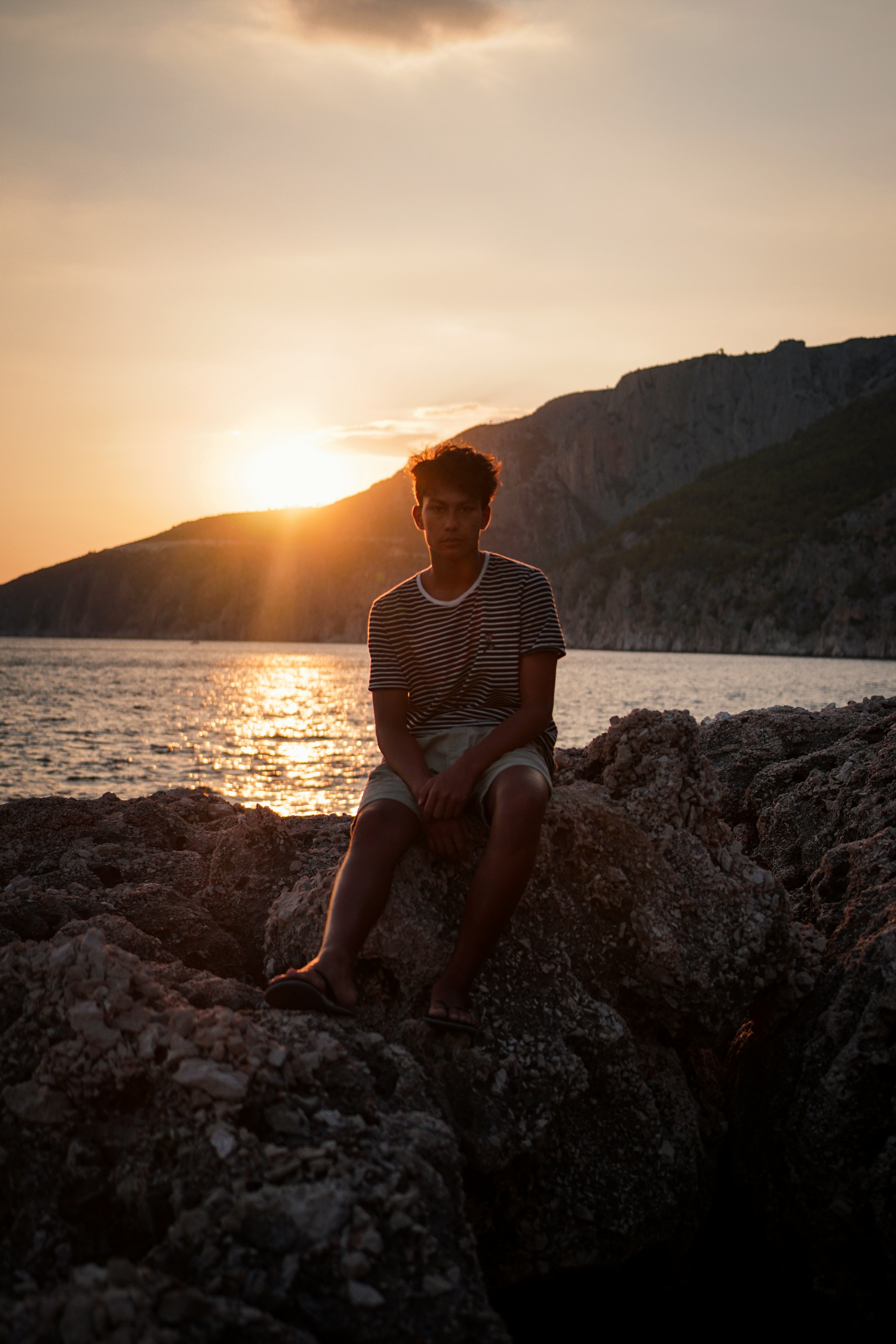 man sitting on rock near sea at golden hour